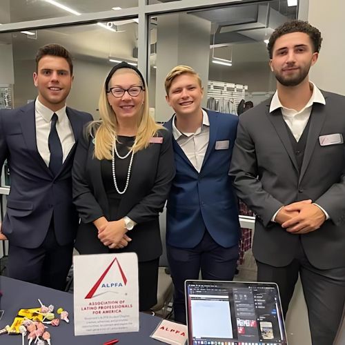 A group of students with the Business Professor advisor at a table for the Association of Latino Professionals for America (ALPHA) to represent how student clubs are part of why Rosemont College is Forbes rated best online college, and a best Main Line college.
