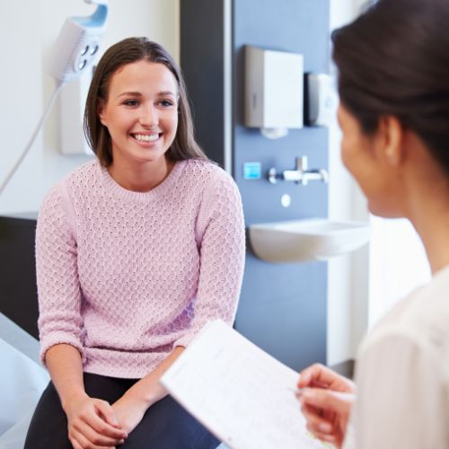 Female patient smiling while seated on a hospital bed and talking with a discharge nurse to represent how student wellness is part of why Rosemont College is a Forbes rated best online college, and a best Main Line college.