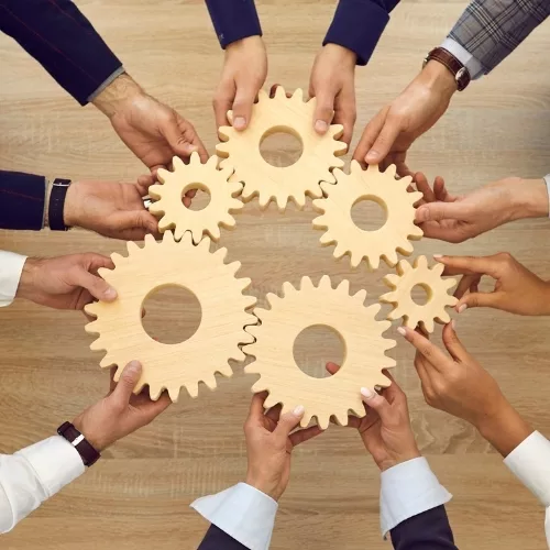 A group of hands holding gears to represent how employees are part of why Rosemont College is a Forbes rated best online college, and a best Main Line college.