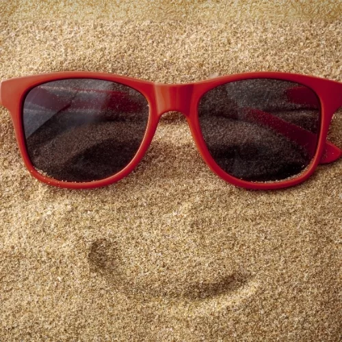Sunglasses on sand with a line made to look like a smile to represent how employees are part of why Rosemont College is a Forbes rated best online college, and a best Main Line college.