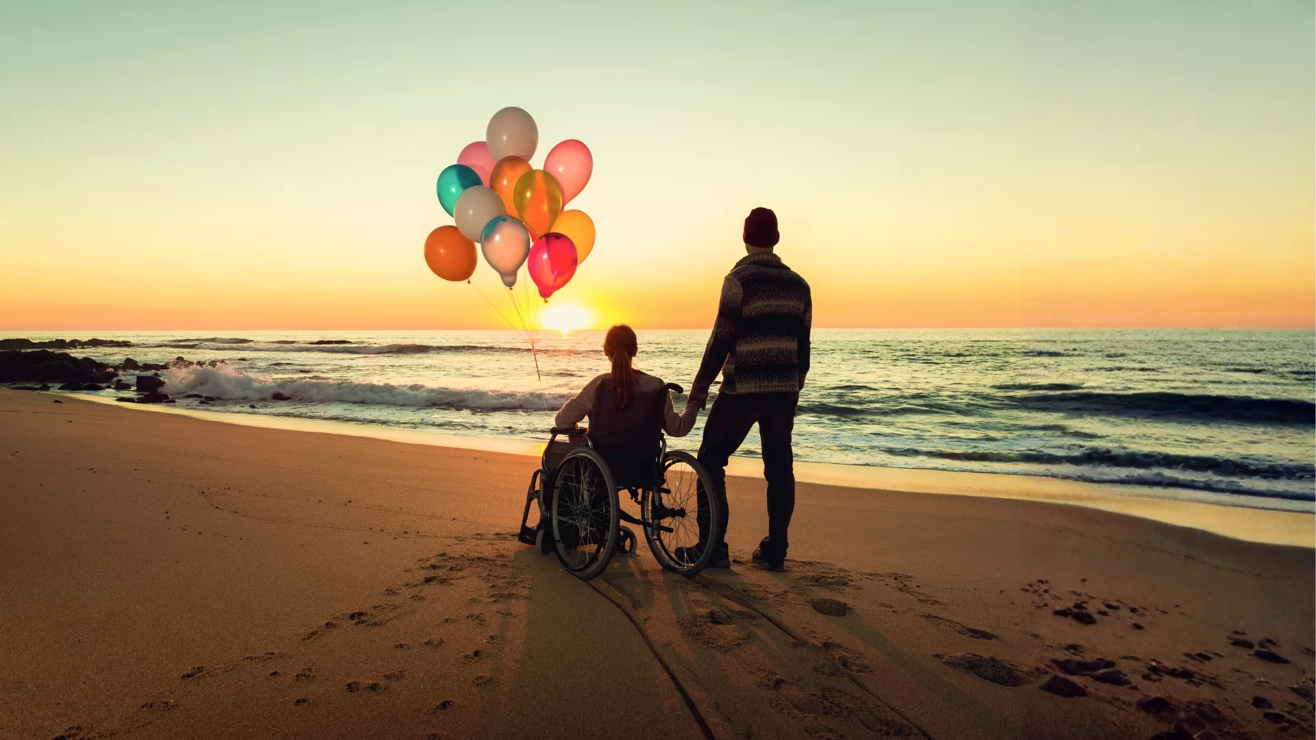 Rosemont College - Writer's Studio Masterclass - Don’t Diss Me I’m Able A woman in a wheelchair with a man and a bouquet of balloons at the beach to represent how the Writer's Studio Young Adult Fiction Disability Inclusiveness Masterclass is part of why Rosemont College is a Forbes rated best online college, and a best Main Line college.