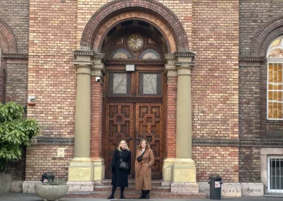 A photograph featuring Dr. Christine Hagedorn & Dr. Lori Hockley standing below the arched entrance to McDaniel College in Budapest is part of why Rosemont College is a Forbes rated best online college, and a best Main Line college.