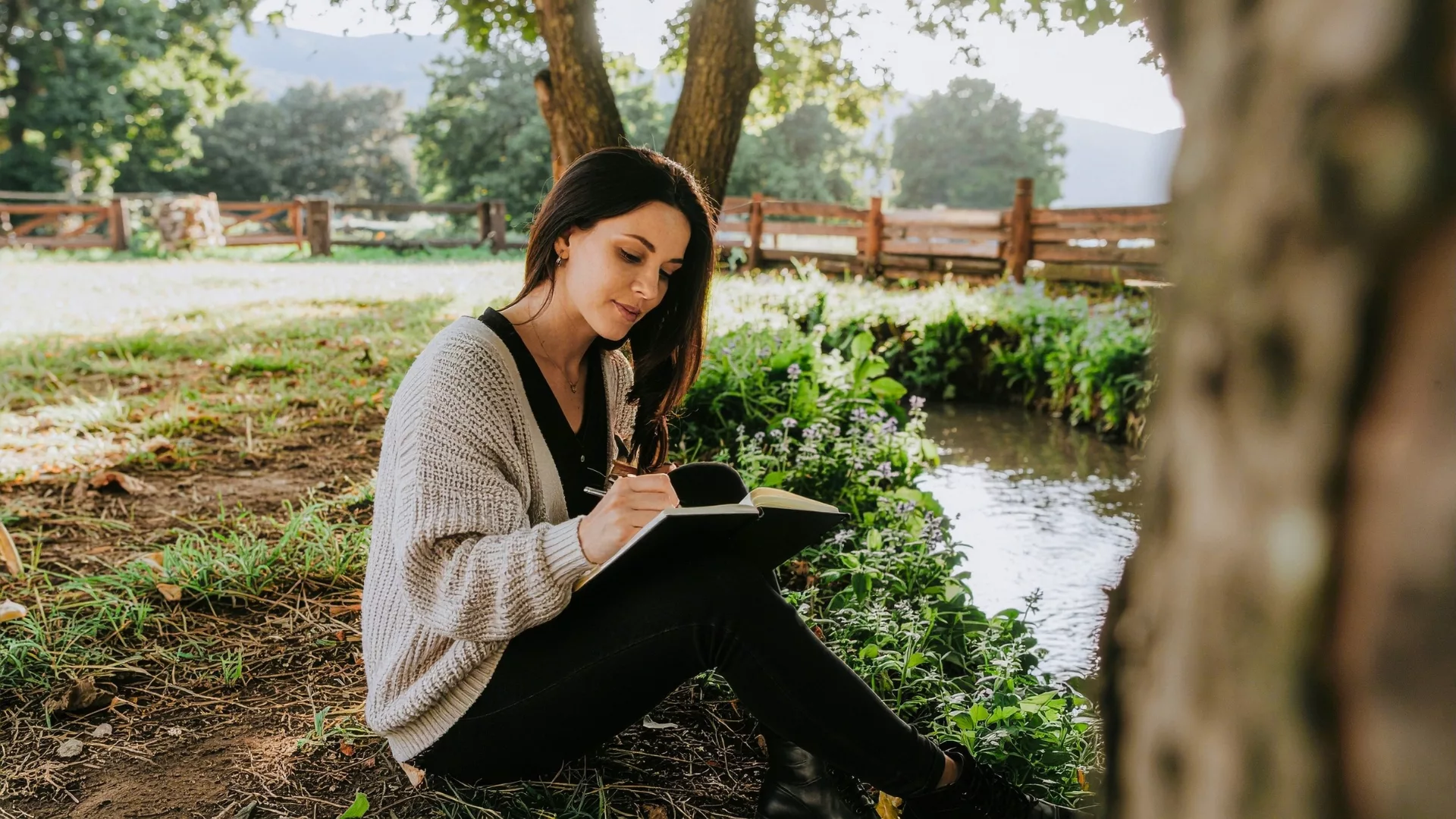 A woman journaling by a brook to represent how Writer's Studio Weekend Retreats are a part of why Rosemont College is a Forbes rated best online college, and a best Main Line college.