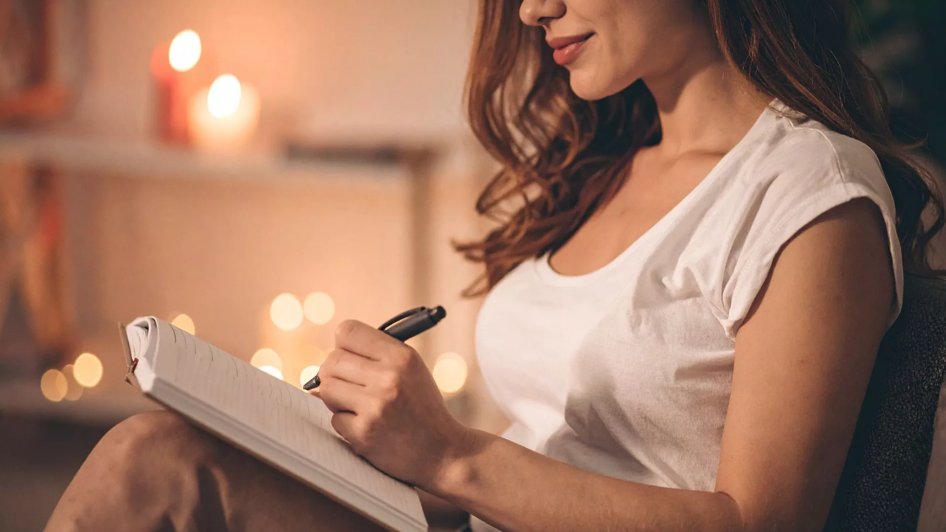 Profile of a woman writing with candles in the background to represent how the The Writer's Studio Weeklong Novel Writing Retreat with Charles Holdefer is a part of why Rosemont College is a best Main Line college.
