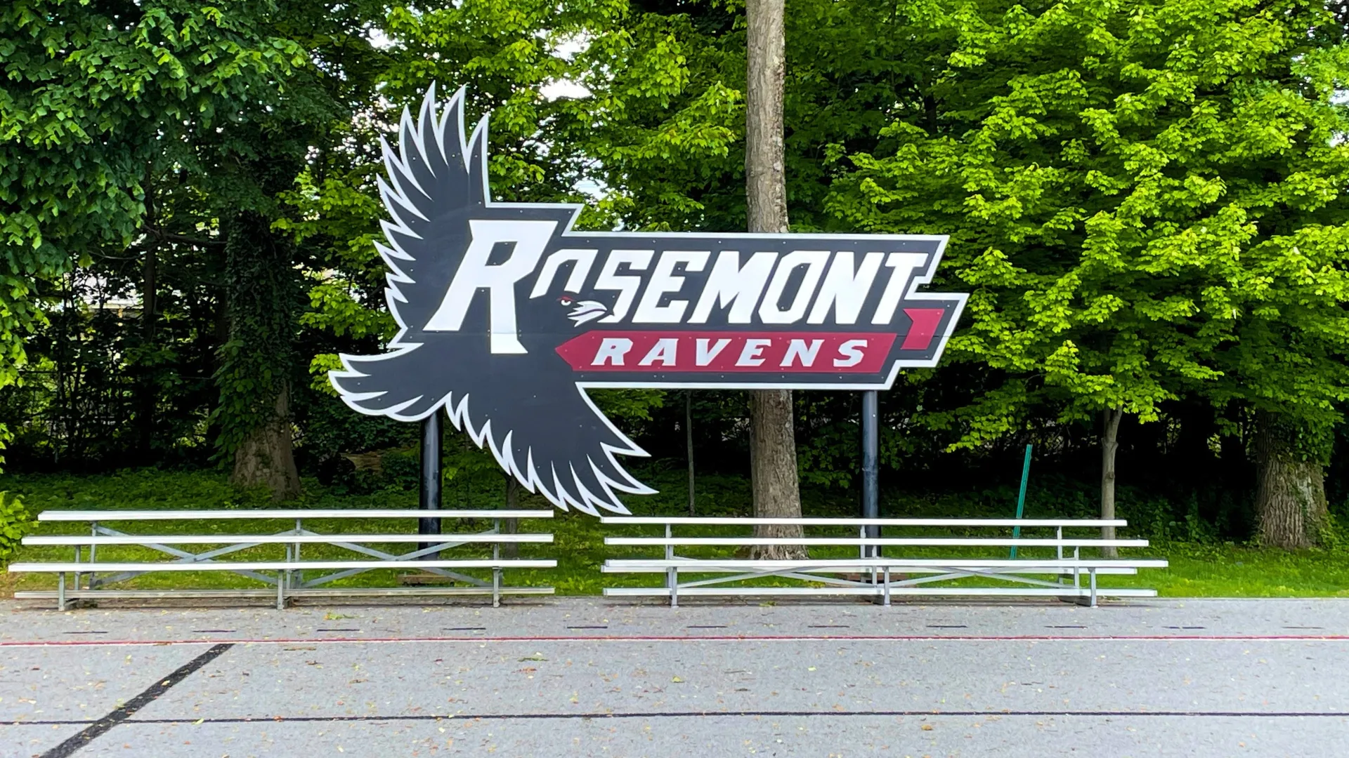 The Rosemont Ravens logo and bleachers on the gray field to represent how the athletics is part of why Rosemont College is a Forbes rated best online college, and a best Main Line college.